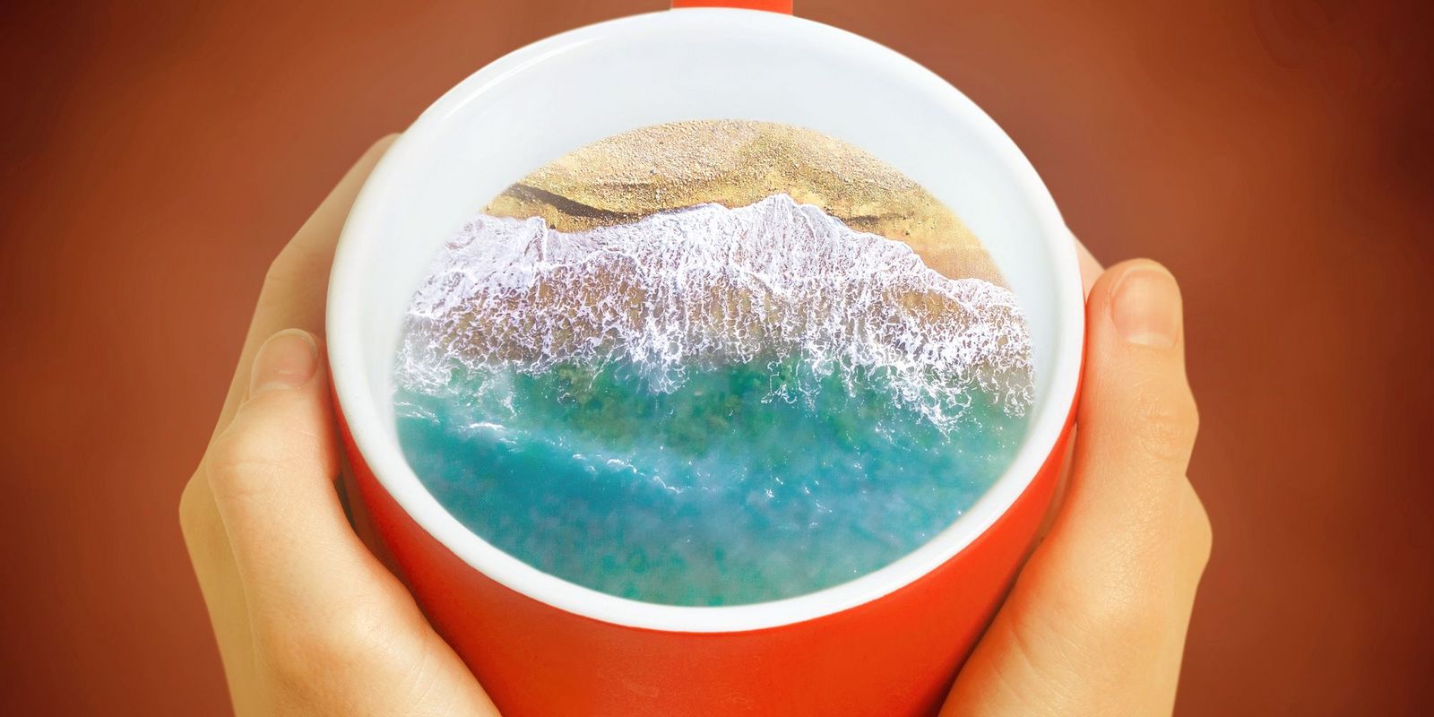 Strand und Berge in Kaffeetasse festgehalten von zwei Händen