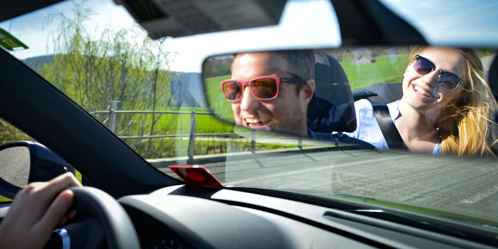 lachendes Paar sitzen in einem fahrenden Auto durch den RĂŒckspiegel fotografiert